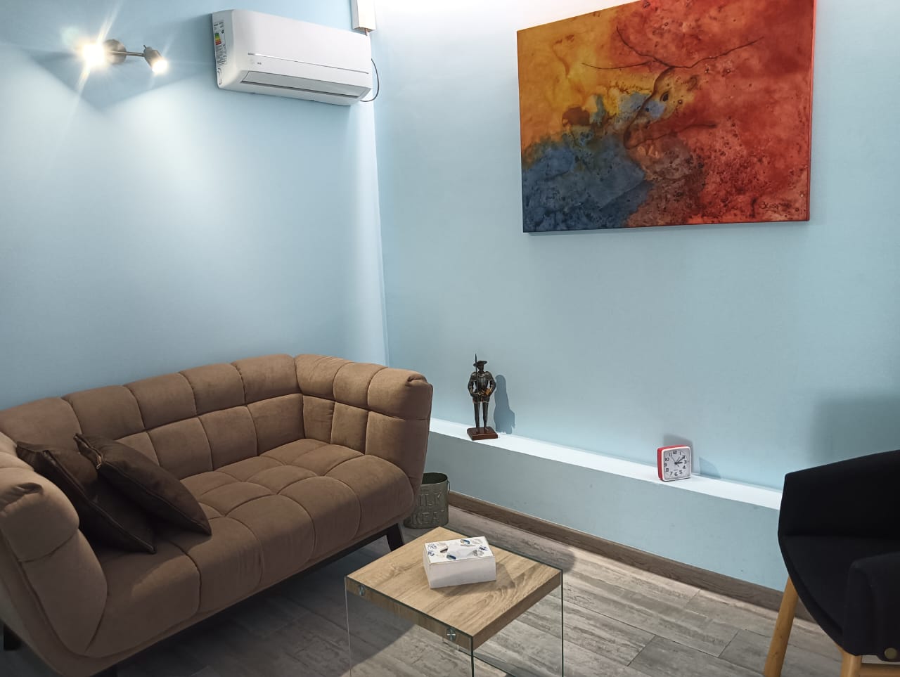 Foto de un box con un sillón de color café y un gran cuadro colgado en la pared
